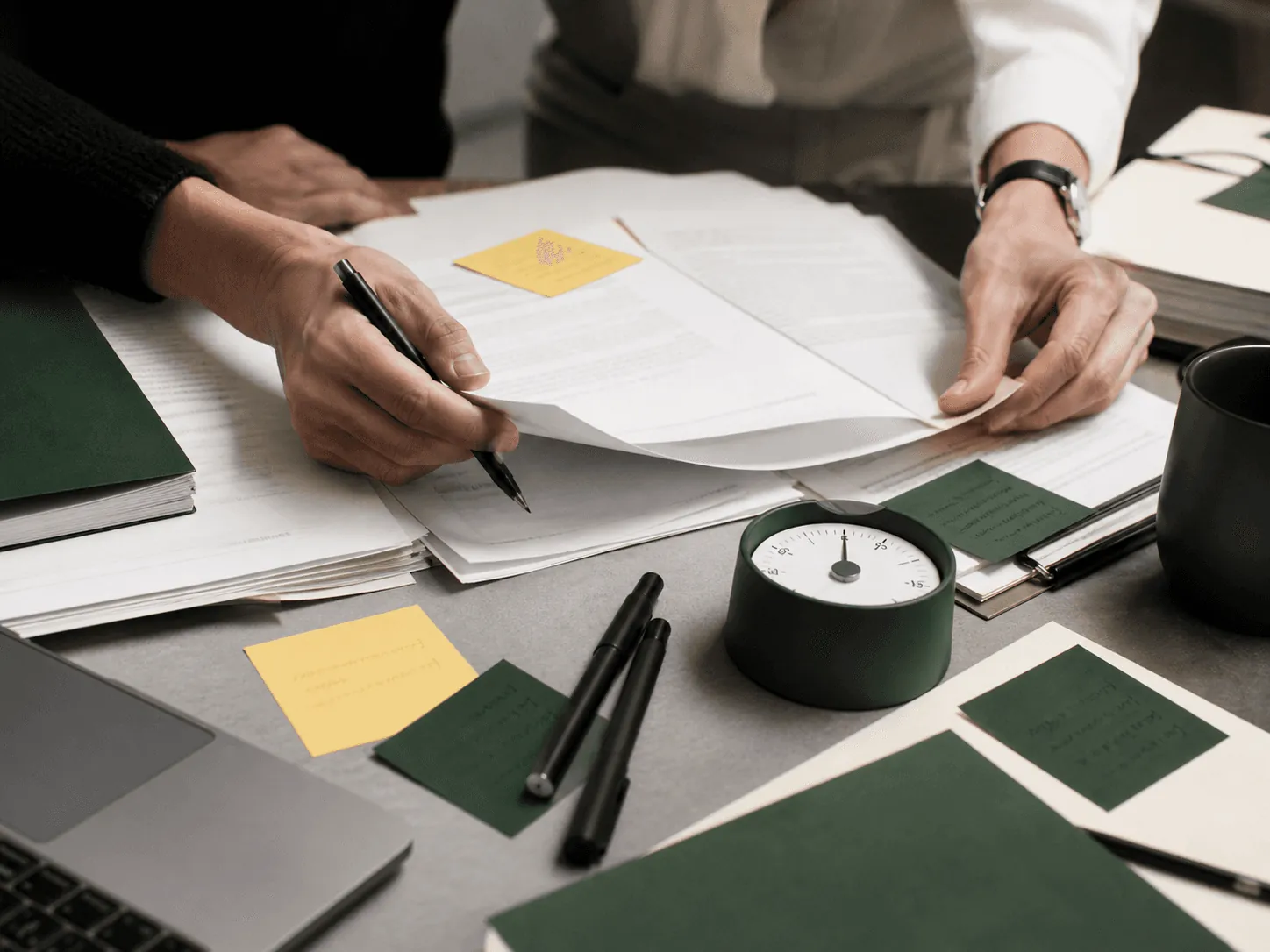 Manos revisando contratos con un temporizador sobre la mesa